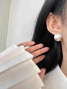 Detail of silver half-ball earrings with brushed matte texture on model's ear