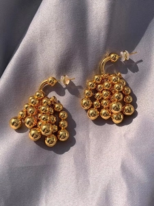 Detail of golden grape cluster drop earrings with shiny beads on silver satin fabric
