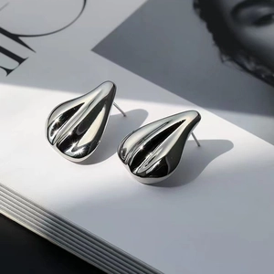 Polished silver teardrop earrings displayed on a fashion magazine with sharp shadows