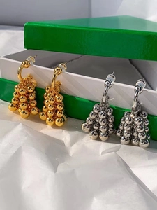 Detailed view of gold and silver grape cluster earrings hanging on a jewelry box