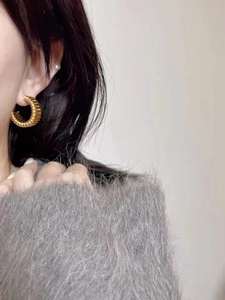Détail de boucles d'oreilles créoles dorées texturées sur un mannequin en pull gris doux