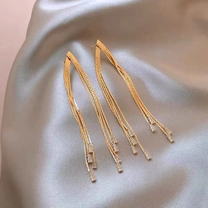 Elegant gold multi-layered tassel earrings with baguette zircons on silk background