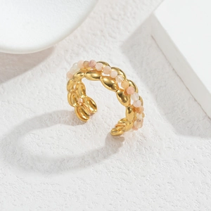Gros plan d'une bague ouverte dorée à deux rangs avec perles roses sur surface en pierre