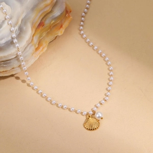 Collier de perles baroques avec pendentif coquillage doré sur fond de sable fin