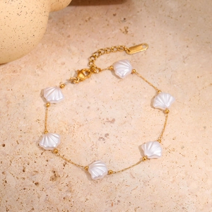 Détail d'un bracelet en acier doré avec six breloques en nacre sur fond en pierre