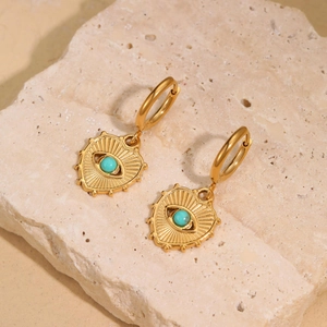 Pair of gold heart earrings with turquoise evil eye detail on travertine stone surface
