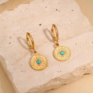 Vintage golden stainless steel hoop earrings with blue eye charms on beige stone