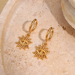 Macro detail of golden evil eye drop earrings on a natural stone textured jewelry tray