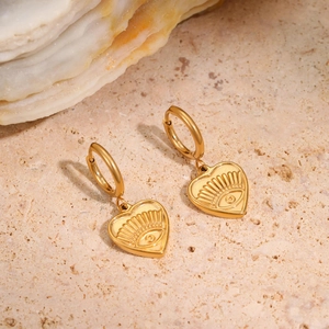 Macro view of gold heart earrings with evil eye engraving on natural stone background