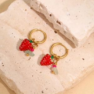 Close-up of 18k gold strawberry earrings with red charms and natural stones