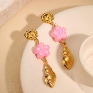 Close-up of 18k gold shell earrings with pink resin flower and rose studs on a ceramic tray
