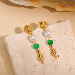 Macro shot of gold seashell earrings with pearl and green beads on a stone