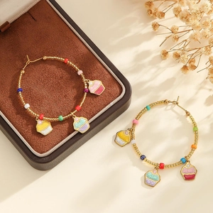 Détail de créoles dorées avec perles colorées et breloques cupcake en émail sur fond chaud