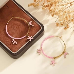 Détail de créoles dorées avec perles roses et breloques marines sur boîte à bijoux