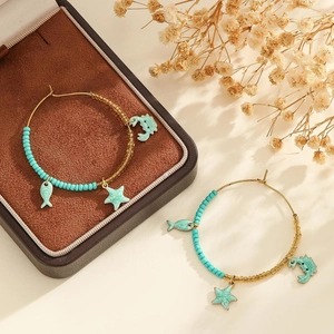 Détail de créoles dorées avec perles turquoise et breloques étoile de mer sur boîte