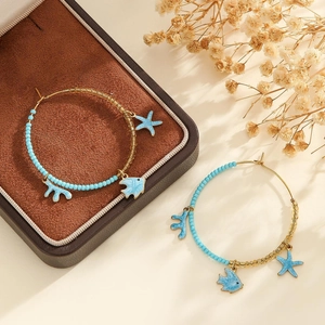 Détail de créoles thème océan avec perles bleues et breloques émaillées étoile de mer