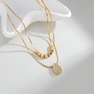 Gold double-layer necklace with heart pendant and metallic beads on a white tray