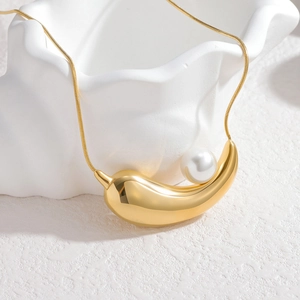Minimalist 18k gold water drop necklace with white pearl on an artistic white pedestal