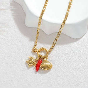 Macro shot of gold necklace with turtle, red chili, and scallop shell pendants on white
