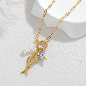 Golden fish pendant necklace with white pearls and blue ceramic bead on a white bust