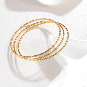 Drie minimalistische 2mm goudkleurige roestvrijstalen armbanden met textuur op witte sokkel