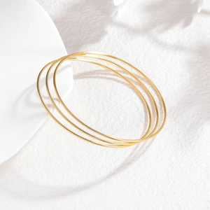 Close-up van drie minimalistische 2mm vergulde roestvrijstalen armbanden op een witte voet