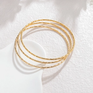 Detail van drie minimalistische goudkleurige roestvrijstalen armbanden met textuur