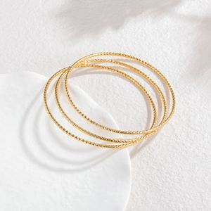 Detail van vier dunne gouden armbanden met diamantgeslepen textuur op wit keramisch bord