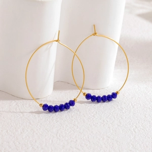 Boucles d'oreilles créoles dorées avec perles bleues à facettes sur support blanc