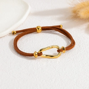 Detailed shot of brown suede cord bracelet with gold organic oval metal clasp on white surface