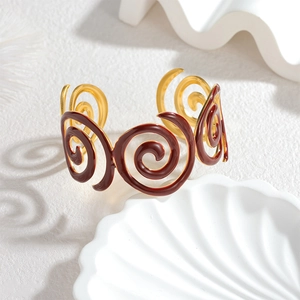 Détail d'un bracelet spirale doré avec émail rouge foncé sur fond de pierre blanche épuré