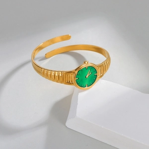Bracelet jonc doré style montre avec cadran vert sur support en marbre blanc élégant