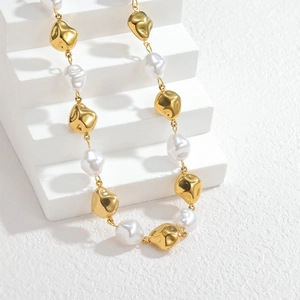 Collier en perles métalliques dorées irrégulières et perles baroques sur socle blanc