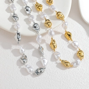 Baroque pearl and liquid metal necklace in gold and silver finish shown on white ceramic