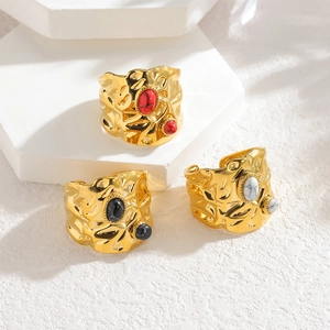Textured irregular gold rings with inset stones displayed on white geometric stones