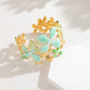 Wide gold open bangle with shell flower enamel designs on a white stone pedestal