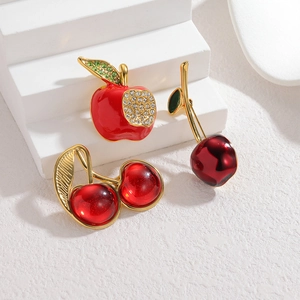 Red apple and cherry fruit brooches with green crystals on white geometric stand