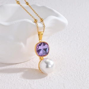 Collier doré avec cristal violet et pendentif perle blanche sur un bol en céramique