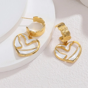 Boucles d'oreilles cœur dorées avec texture tressée et nacre blanche sur socle blanc