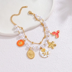 Double-layered 18k gold plated bracelet with pearls and various floral charms on marble