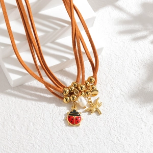 Détail du collier multicouche en daim brun avec pendentifs libellule et coccinelle
