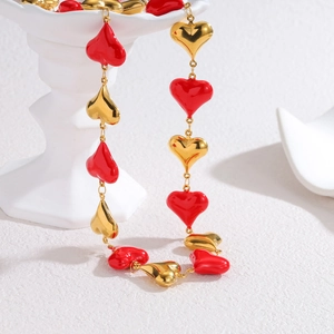 Elegant gold and red enamel heart link necklace displayed on a white classical pillar stand