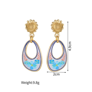 Detailed view of 18k gold floral oval earrings with white enamel and blue flower art