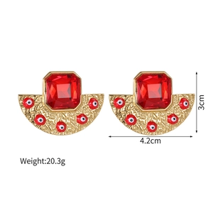 Macro detail of red rectangle crystal and fan-shaped evil eye drop earrings in 18k gold