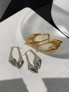 Detailed view of polished gold and silver water drop earrings on white textured leather