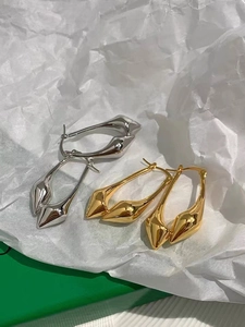 Minimalist teardrop earrings in polished gold and silver on artistic white paper