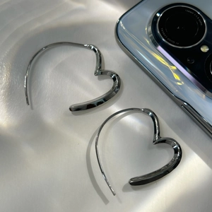 Minimalist irregular heart-shaped silver hoop earrings shown on white silk fabric