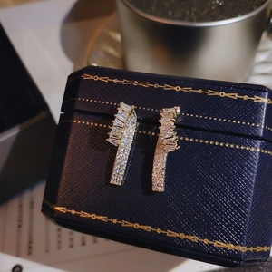 Boucles d'oreilles dorées ondulées avec zircons sertis sur un écrin à bijoux bleu