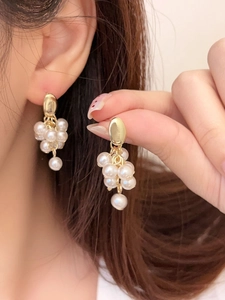 Detailed view of elegant gold cluster earrings featuring white pearls in a grape bunch design