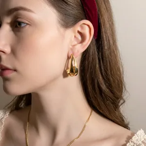 Polished gold geometric hoop earrings with a modern minimalist curved design on a model
